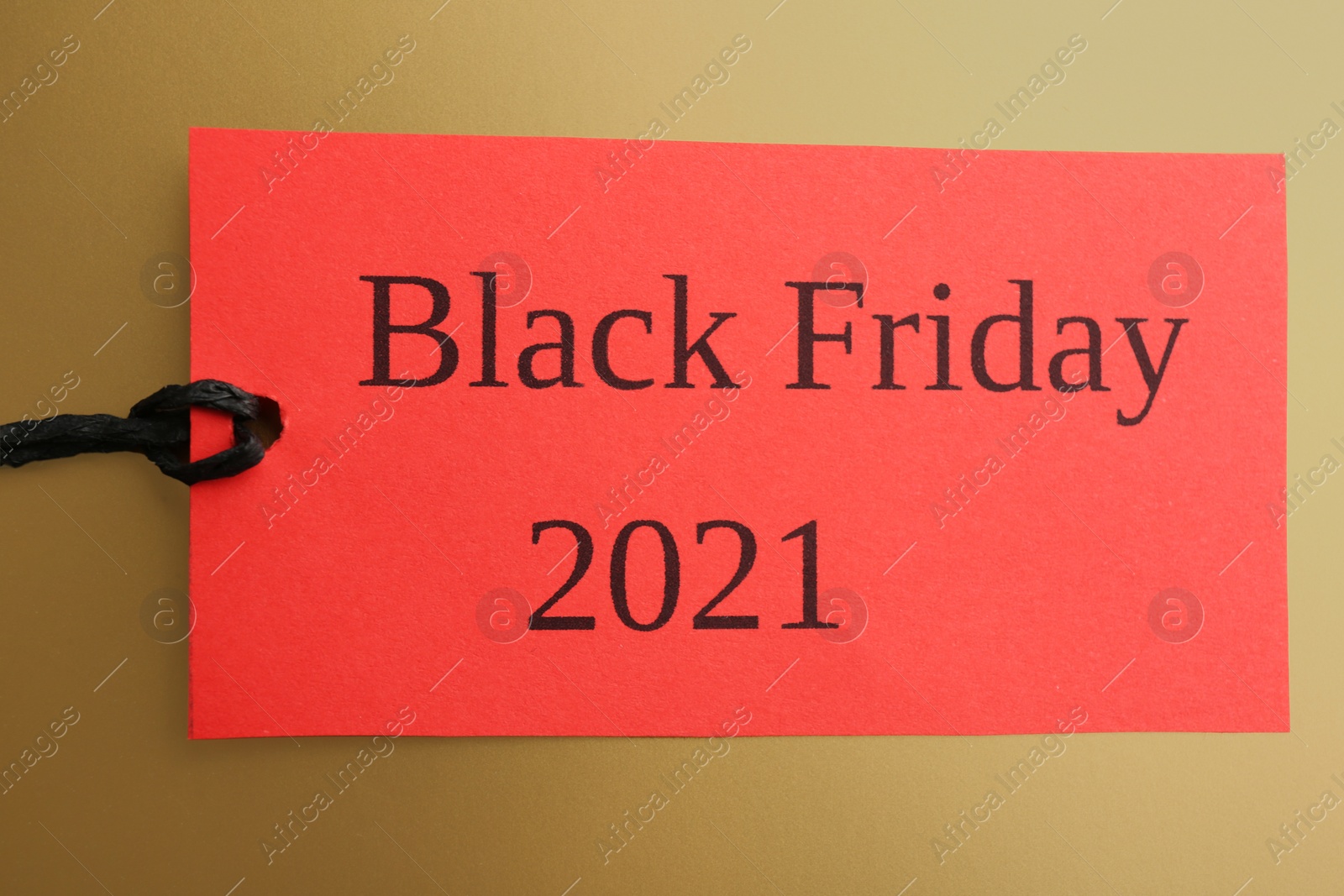 Photo of Red tag with words BLACK FRIDAY 2021 on golden background, top view