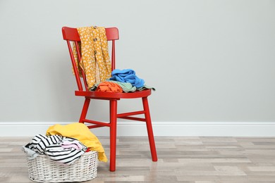 Photo of Red chair and wicker basket with different clothes near grey wall, space for text
