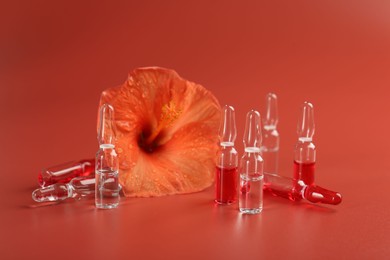 Photo of Skincare ampoules and hibiscus flower on coral background