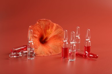 Skincare ampoules and hibiscus flower on coral background