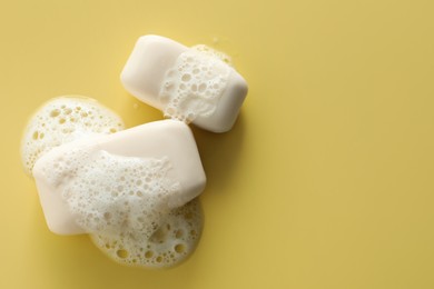 Soap bars with fluffy foam on yellow background, flat lay. Space for text