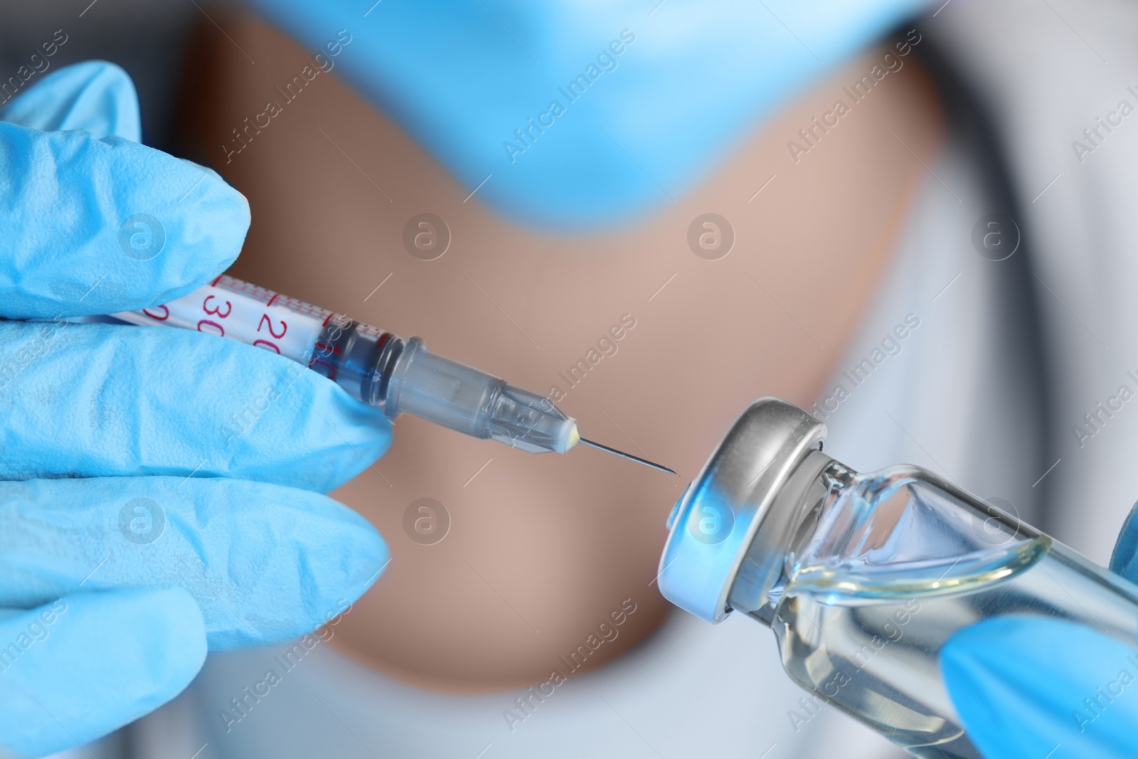 Photo of Doctor inserting syringe into glass vial with medication, closeup