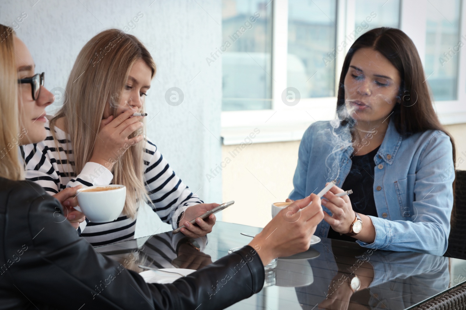 Photo of Women smoking cigarette at table in outdoor cafe