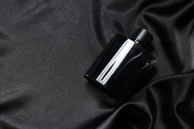 Photo of Luxury men's perfume in bottle on black satin fabric, above view. Space for text