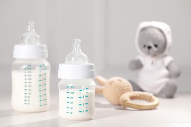 Photo of Feeding bottles with milk and toys on white wooden table. Space for text
