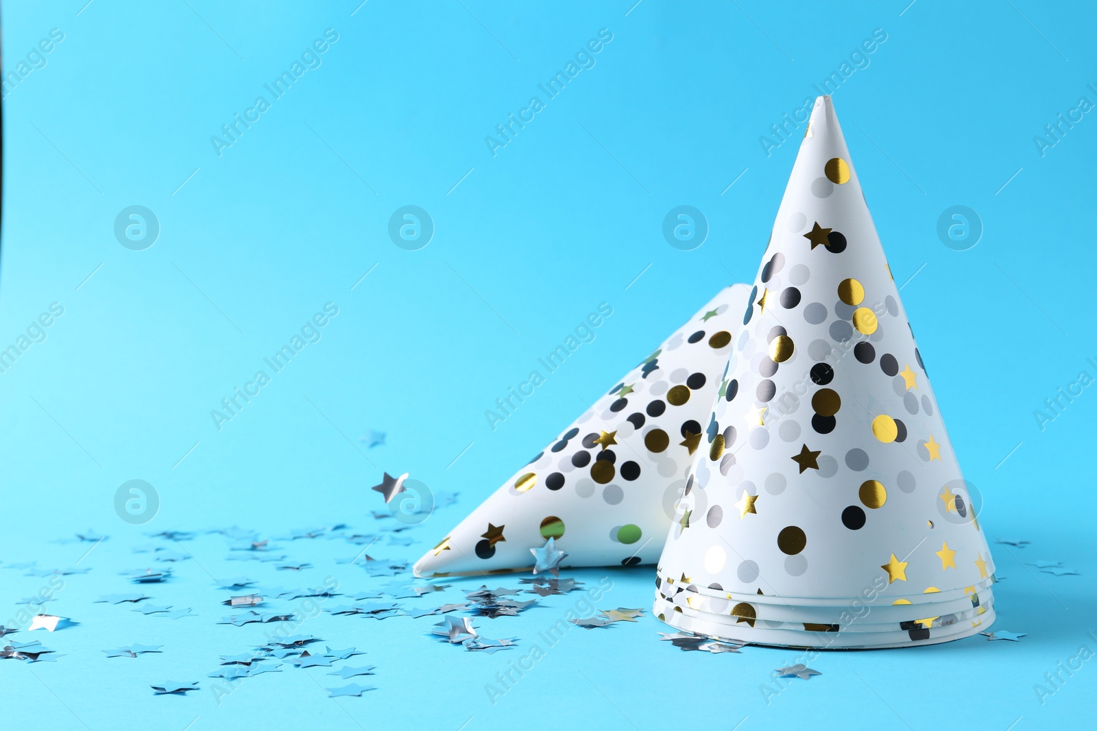 Photo of Party hats and confetti on light blue background, space for text