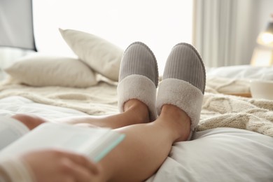 Photo of Woman in soft comfortable slippers reading book on bed at home, closeup