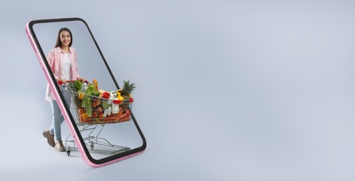 Image of Online purchases. Woman with shopping cart full of different products walking through smartphone on grey background. Banner design with space for text