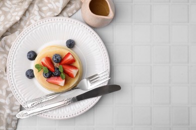 Photo of Delicious pancakes with strawberries, blueberries and mint served on white tiled table, top view. Space for text