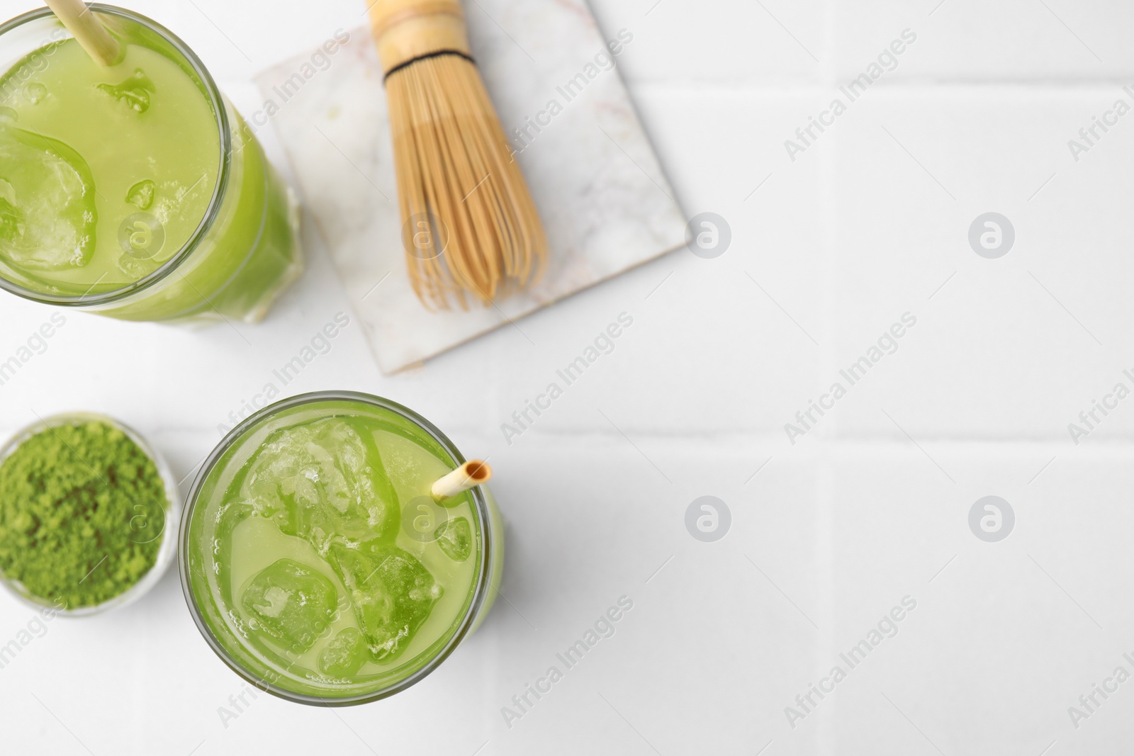 Photo of Delicious iced green matcha tea, powder and bamboo whisk on white tiled table, flat lay. Space for text