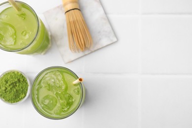 Delicious iced green matcha tea, powder and bamboo whisk on white tiled table, flat lay. Space for text