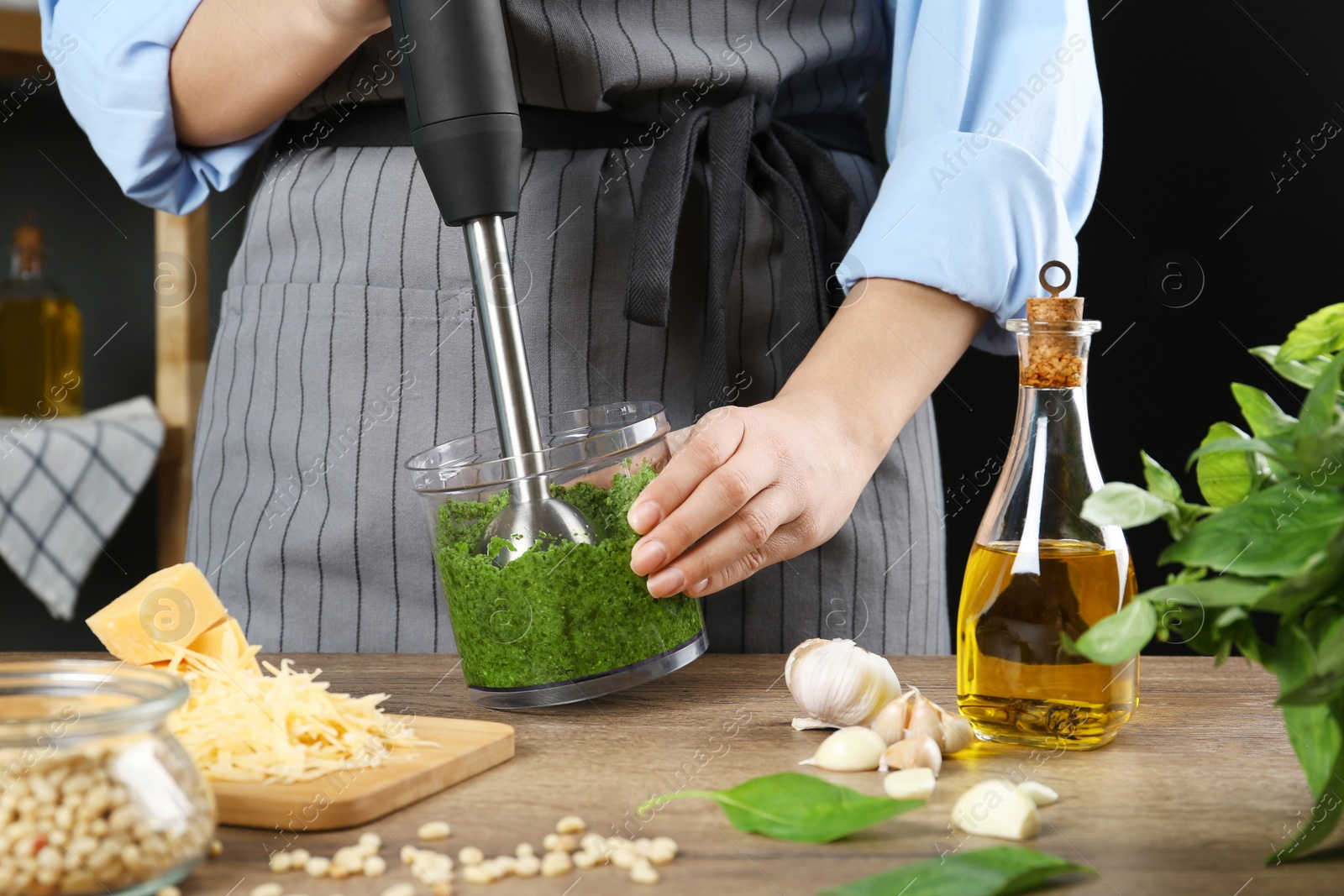 Photo of Woman blending pesto sauce in bowl at table, closeup