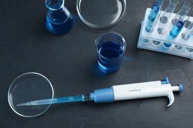 Photo of Laboratory analysis. Micropipette, petri dishes, beaker, flask and test tubes on black table, above view