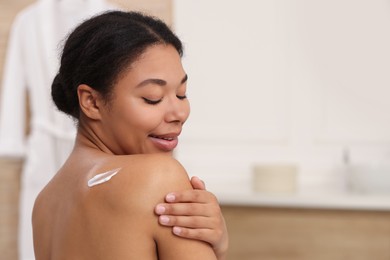 Photo of Young woman applying body cream onto back in bathroom. Space for text