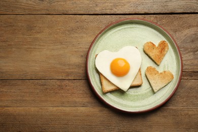 Photo of Plate with heart shaped fried egg and toasts on wooden table, top view. Space for text