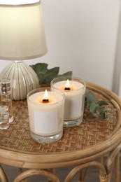 Photo of Burning soy candles, lamp, perfumes and eucalyptus branch on wicker table indoors