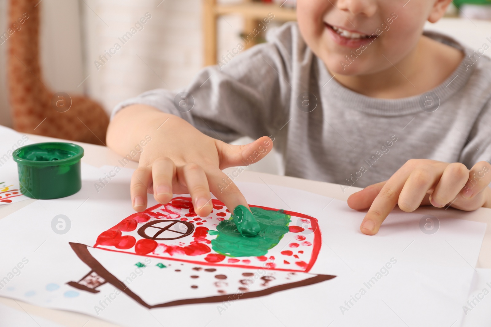 Photo of Little boy painting with finger at white table indoors, closeup