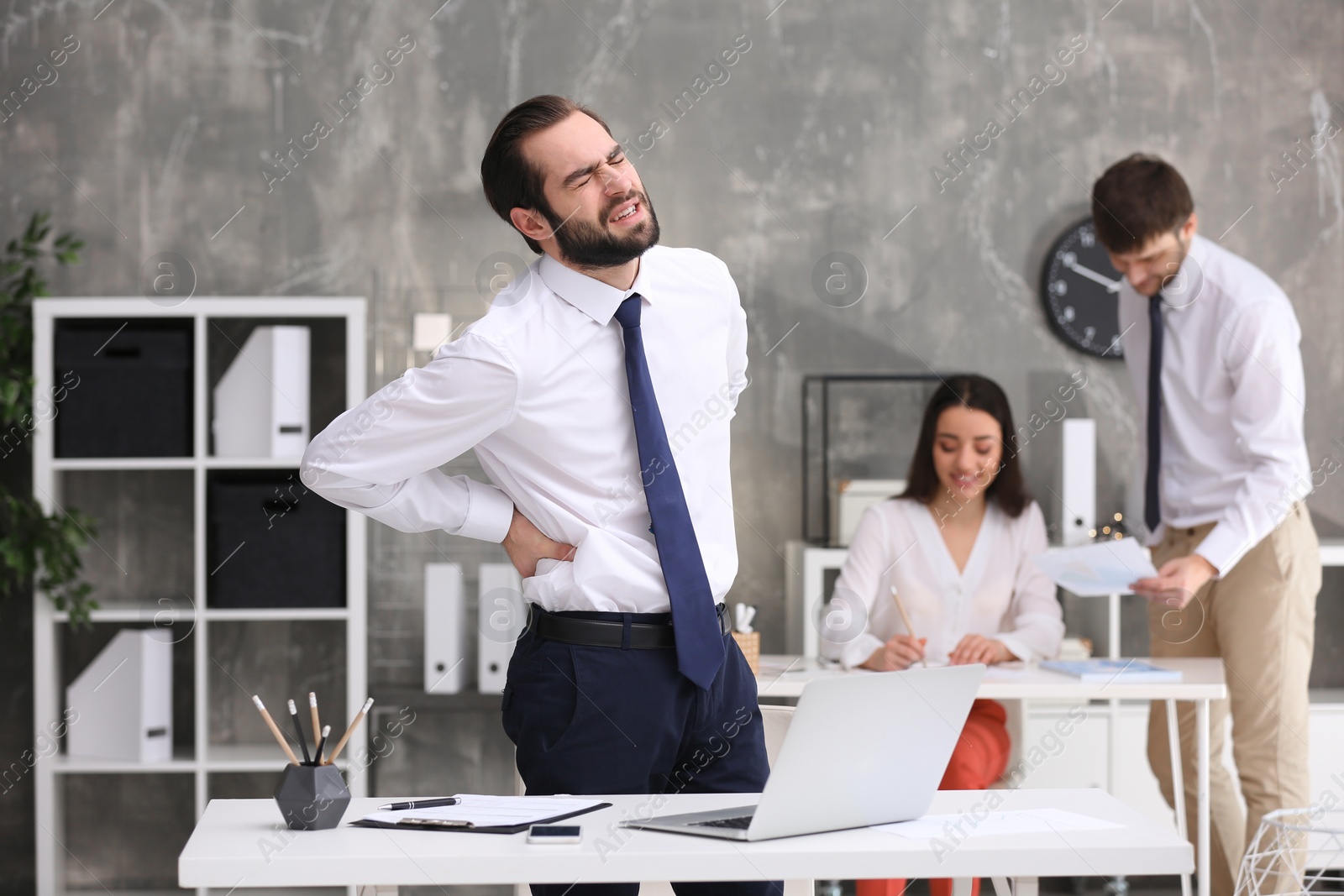 Photo of Young man suffering from back pain in office