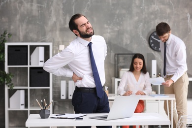 Photo of Young man suffering from back pain in office