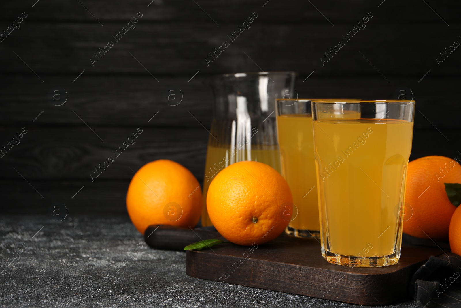 Photo of Many ripe oranges and fresh juice on dark grey table, space for text