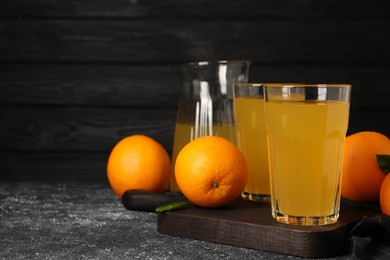 Many ripe oranges and fresh juice on dark grey table, space for text