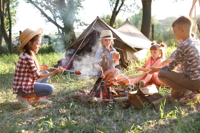 Little children frying sausages on bonfire. Summer camp