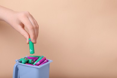 Photo of Woman putting used AA size battery into recycling bin on beige background, closeup. Space for text