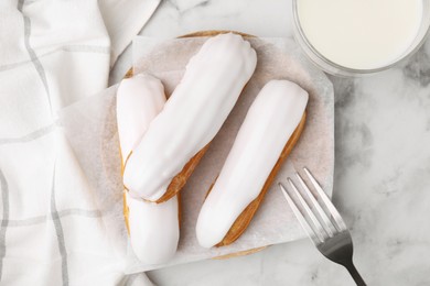 Photo of Delicious eclairs covered with glaze on white marble table, flat lay