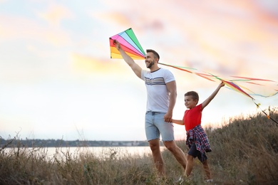 Photo of Happy father and his child playing with kites outdoors at sunset. Spending time in nature
