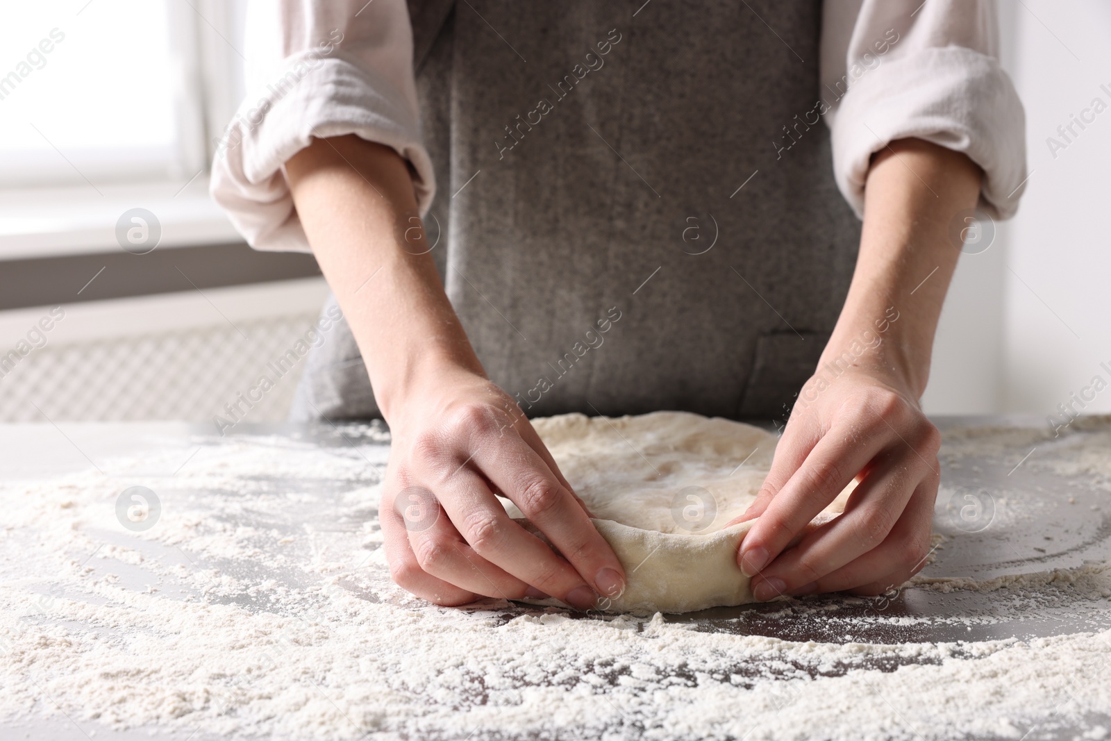 Photo of Woman kneading dough at table in kitchen, closeup