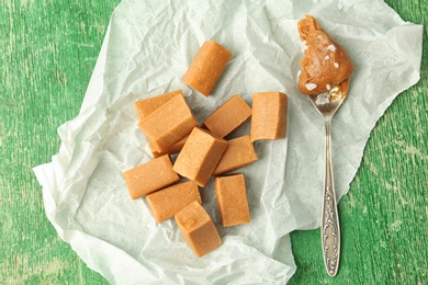 Photo of Delicious candies and salted caramel sauce in spoon on wooden table, top view