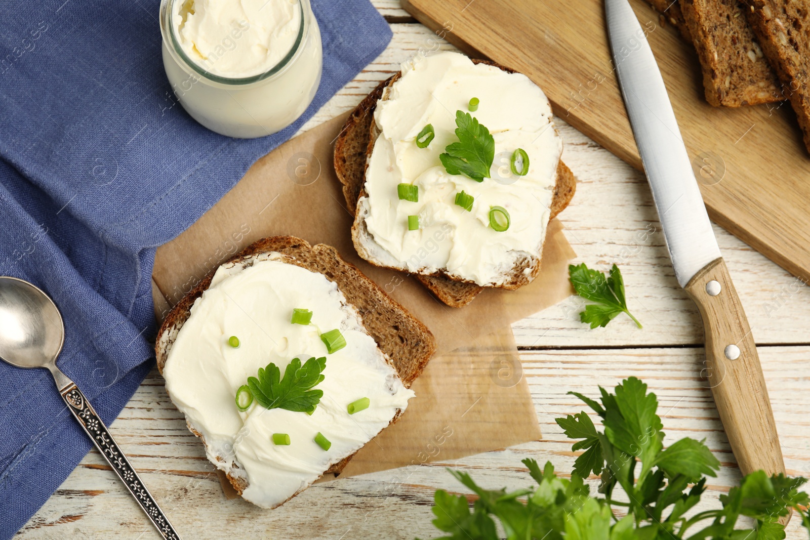 Photo of Bread with cream cheese, green onion and parsley on white wooden table, flat lay