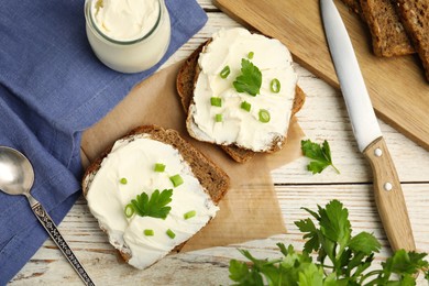 Bread with cream cheese, green onion and parsley on white wooden table, flat lay