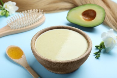 Photo of Homemade hair mask, ingredients and brush on light blue background