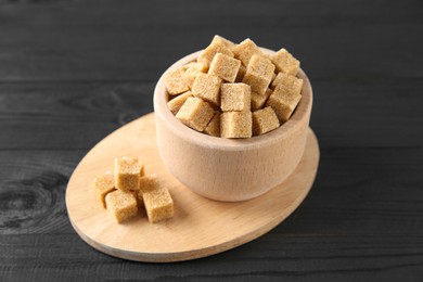 Photo of Brown sugar cubes in bowl on black wooden table