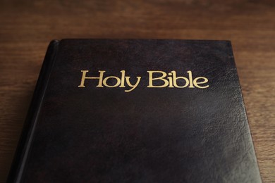 Photo of Hardcover Bible on wooden table, closeup. Religious book