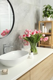 Photo of Vase with beautiful pink tulips and toiletries near sink in bathroom