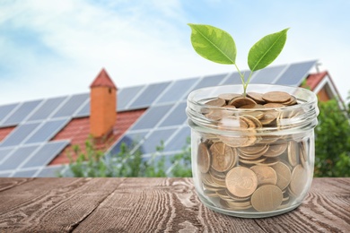 Image of Glass jar with coins and plant against house with installed solar panels on roof. Economic benefits of renewable energy