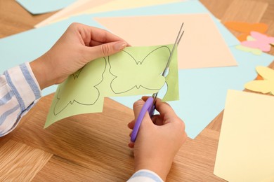 Woman cutting color paper with scissors at wooden table, closeup