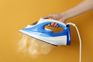 Woman holding modern iron with steam on orange background, closeup