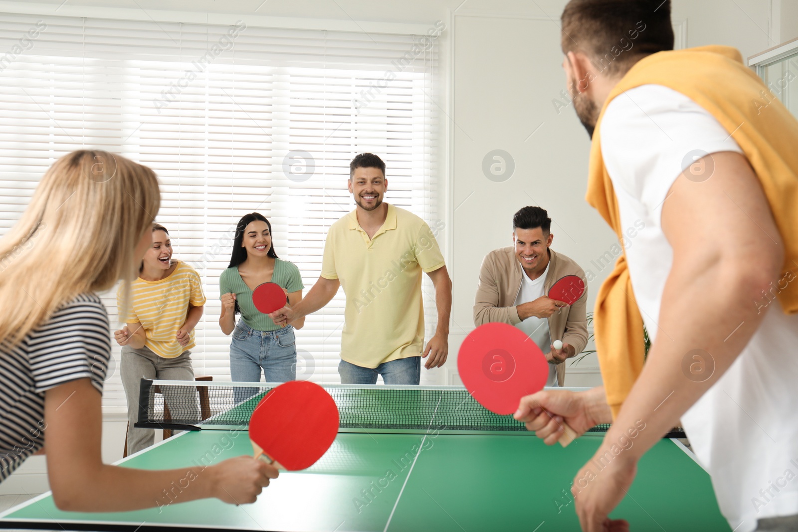 Photo of Happy friends playing ping pong together indoors