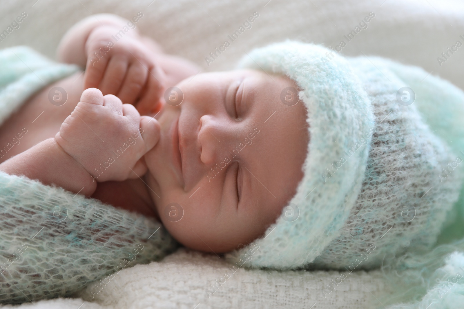 Photo of Cute newborn baby in warm hat lying on white plaid, closeup