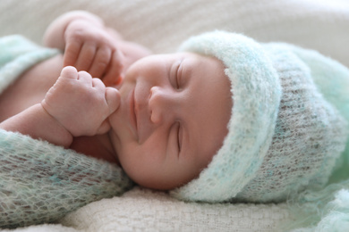 Photo of Cute newborn baby in warm hat lying on white plaid, closeup