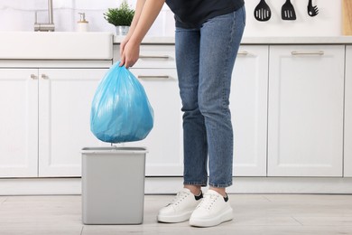 Photo of Woman taking garbage bag out of trash bin in kitchen, closeup