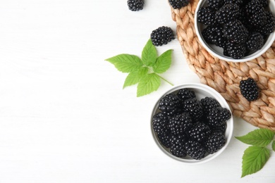 Bowls of ripe blackberries on white wooden table, flat lay. Space for text