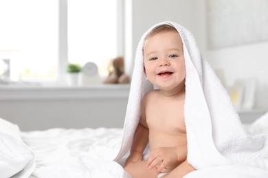 Adorable little baby with towel on bed at home