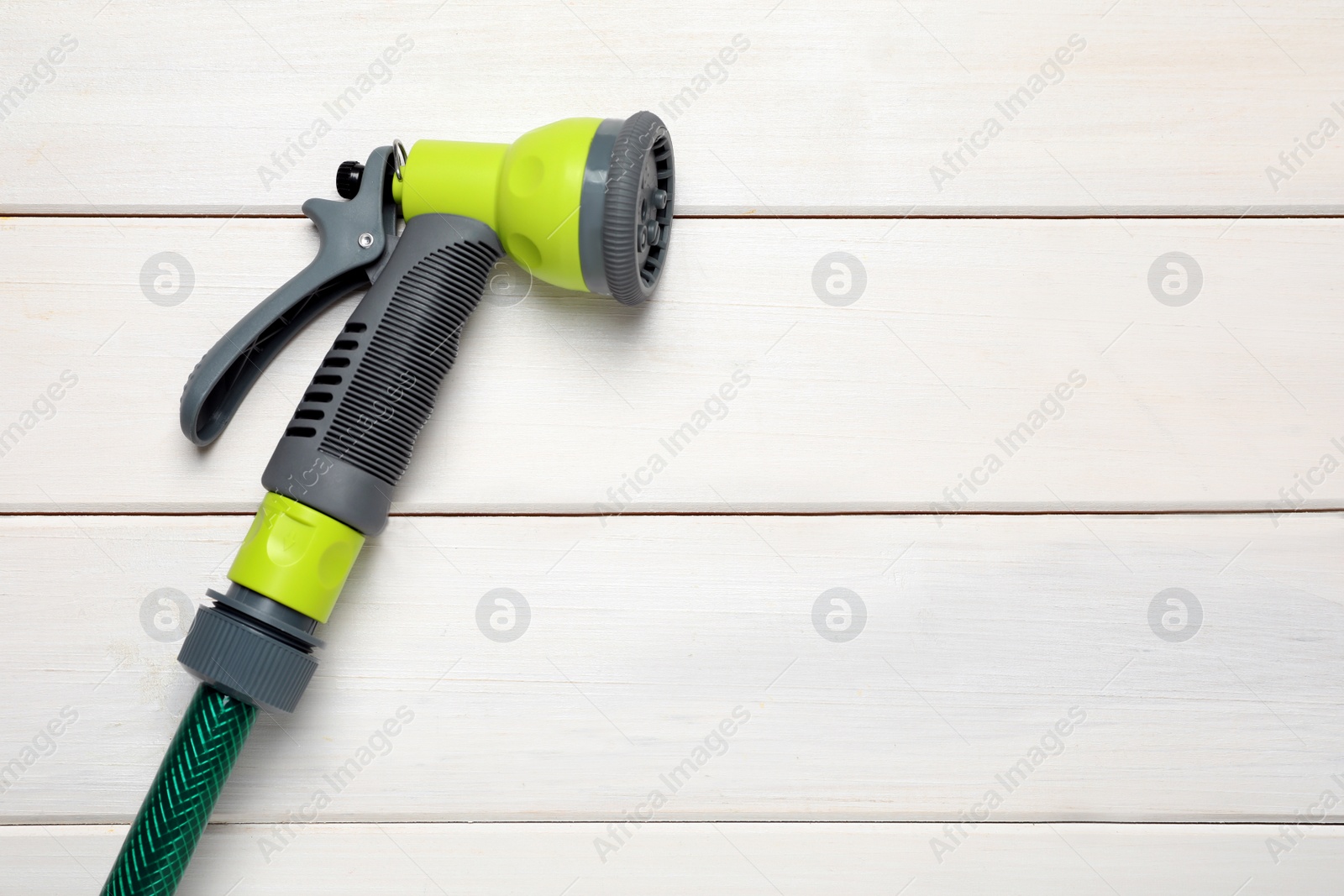 Photo of Green garden hose with spray gun on white wooden table, top view. Space for text