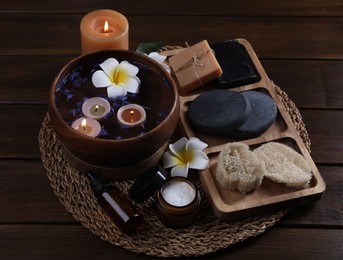 Beautiful composition with different spa products, plumeria flowers and burning candles on wooden table