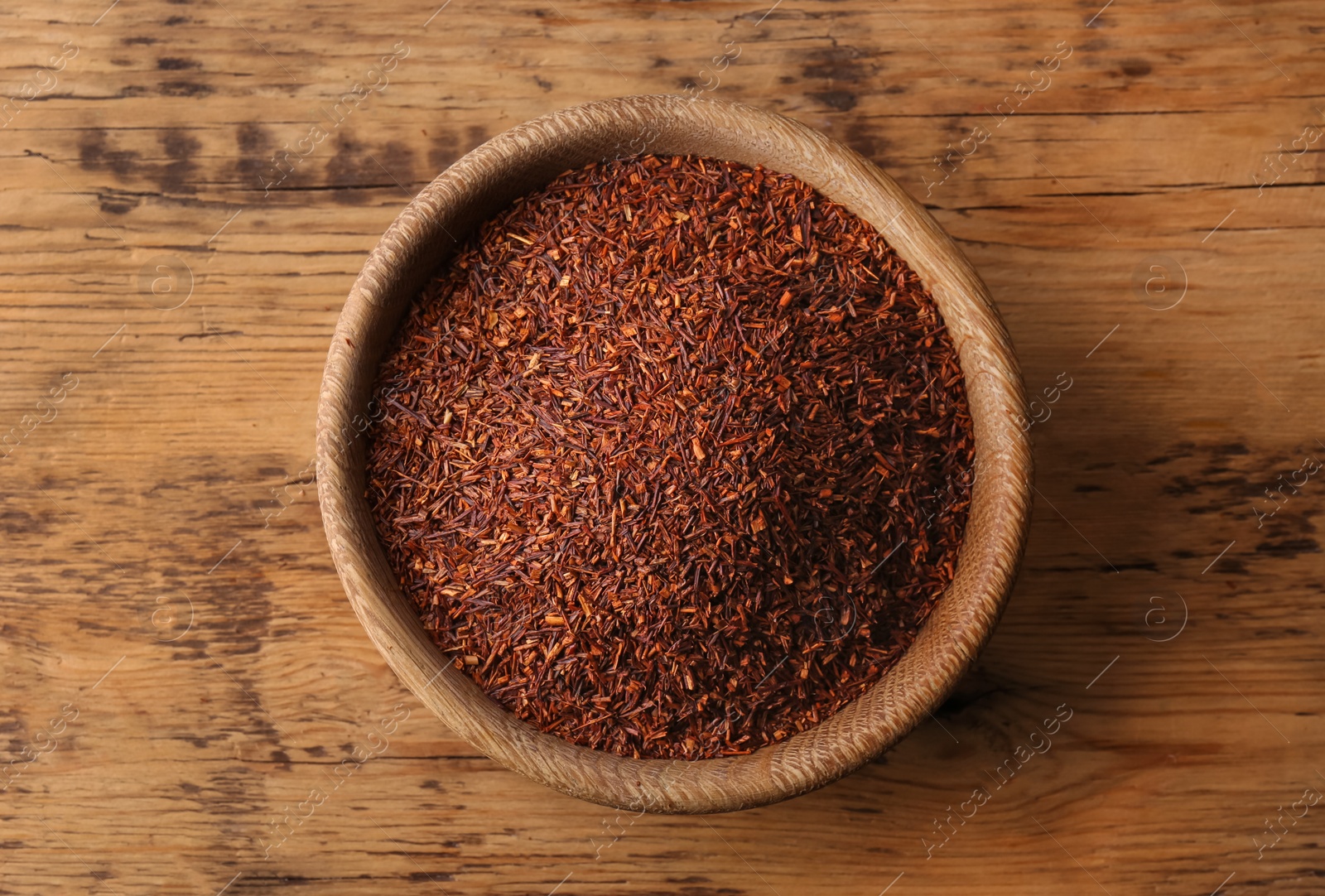 Photo of Dry rooibos leaves in bowl on wooden table, top view