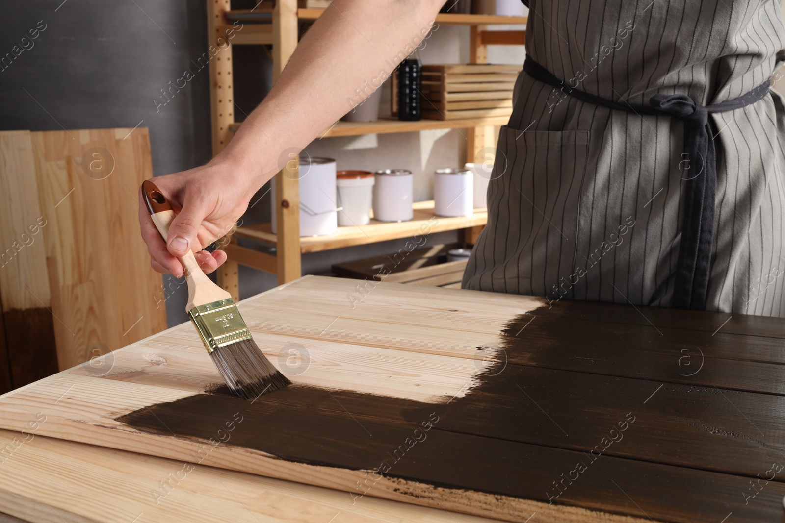 Photo of Man with brush applying wood stain onto wooden surface indoors, closeup